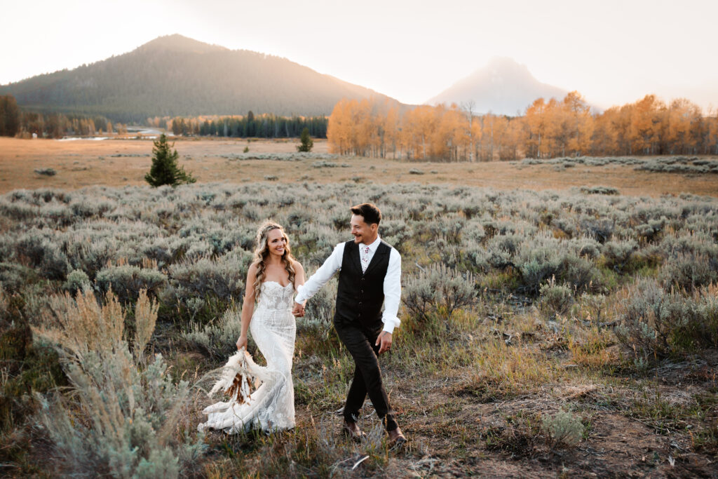 A newlywed couple walk through sage brush at Oxbow Bend in Jackson Hole
